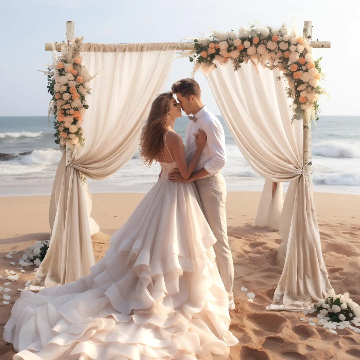 Un couple s'embrasse dans une robe de mariée et un costume devant une décoration florale drapée sur une plage.