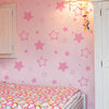 A pink wall decorated with star-shaped vinyl decals for kids, next to a white door and a bed with a colorful patterned sheet.