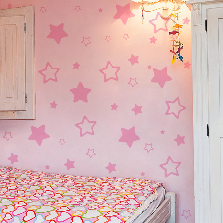 A pink wall decorated with star-shaped vinyl decals for kids, next to a white door and a bed with a colorful patterned sheet.