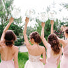 Five women raise floral message wedding thank you signs in a green outdoor setting.