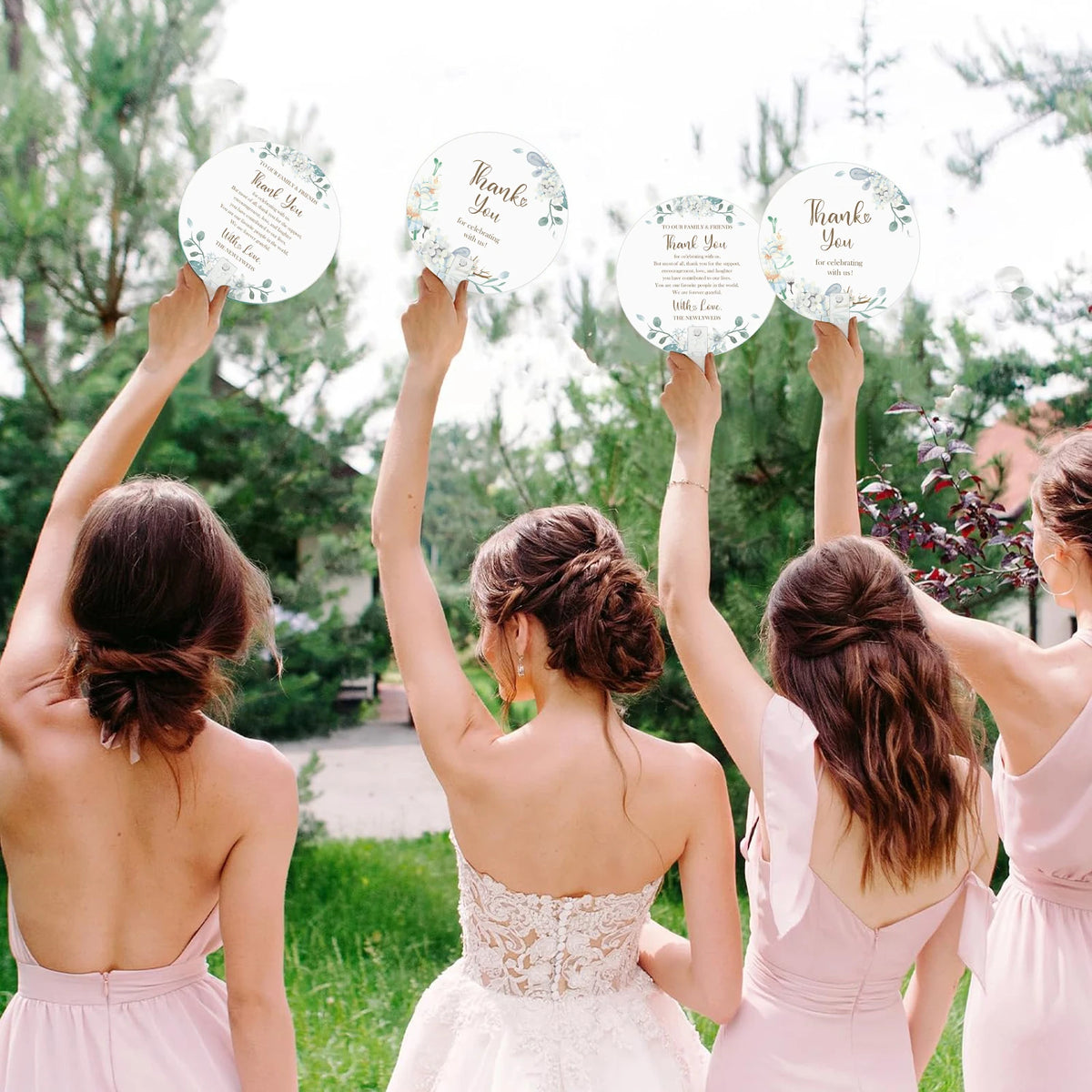 Five women raise floral message wedding thank you signs in a green outdoor setting.