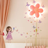 A young girl is interacting with butterfly wall stickers on a wall decorated with pink and purple flowers.
