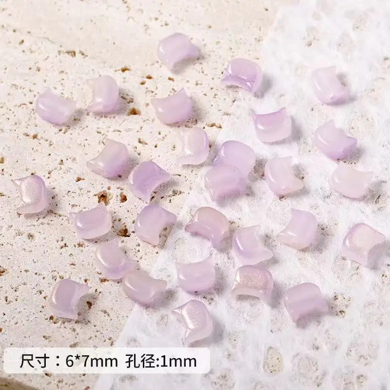 A collection of small, translucent lavender glass beads shaped like cat heads for jewelry making