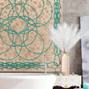A tall vase holds white artificial reed stems against a textured wall with green decorative metalwork.