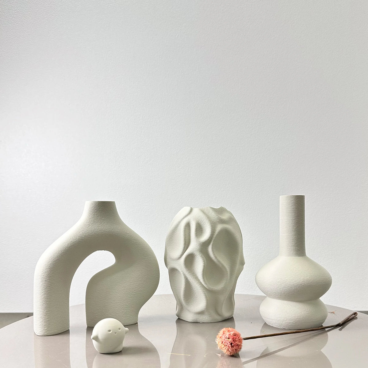 A set of three white ceramic geometric vases with textured surfaces displayed on a light surface.