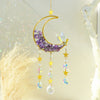 A handcrafted gold moon crystal suncatcher featuring a purple amethyst crescent and dangling prism pendants.