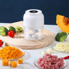 A white portable electric mini food chopper jar filled with chopped vegetables and garlic, placed on a wooden cutting board.