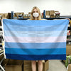 A person holds up a horizontal blue, white, and light blue striped flag banner.