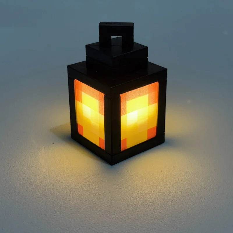 A black pixel style night light lantern with an orange glow sits on a light surface.
