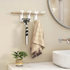 A set of four self-adhesive wall hooks is mounted on a wooden bar, with a towel hanging nearby above a white sink.