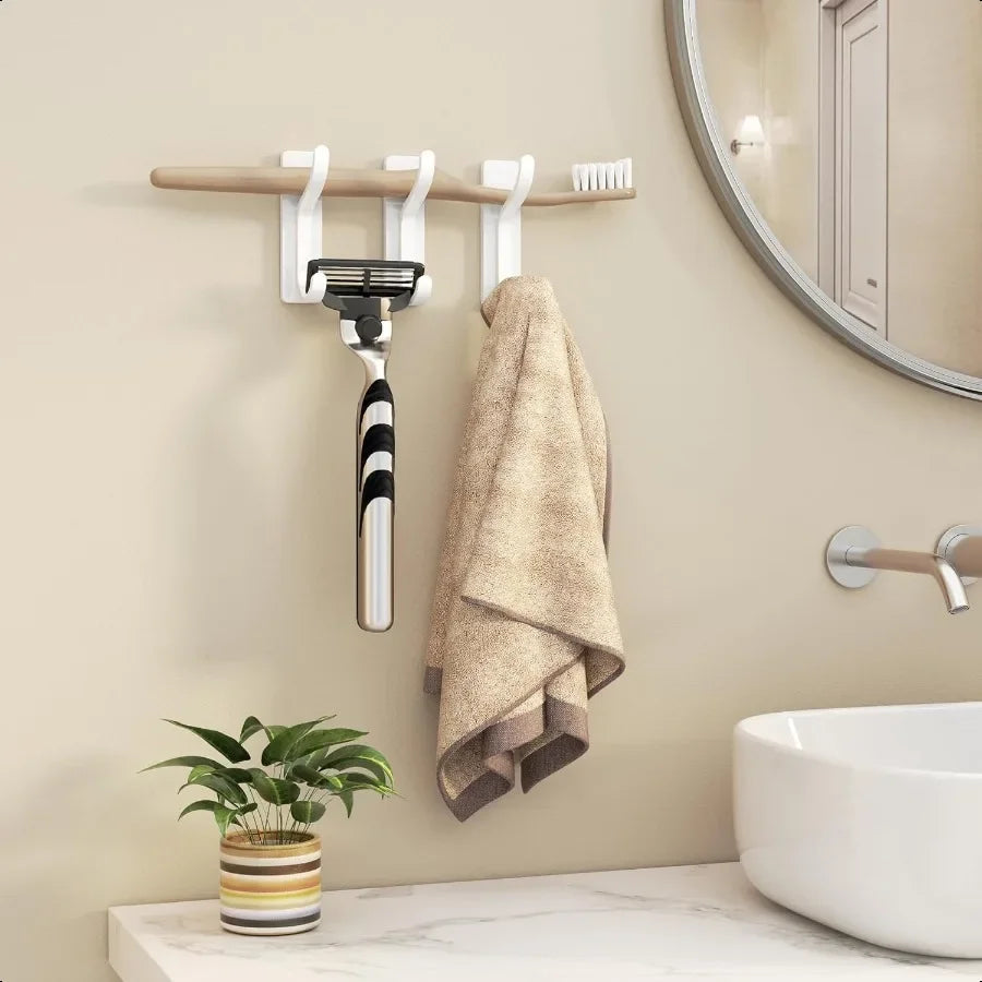 A set of four self-adhesive wall hooks is mounted on a wooden bar, with a towel hanging nearby above a white sink.