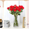 A bouquet of vibrant red velvet artificial roses with bendable stems displayed in a clear glass vase.