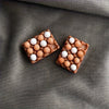 A set of brown chocolate-coated candies with white centers arranged in a diamond shape on a gray fabric background.