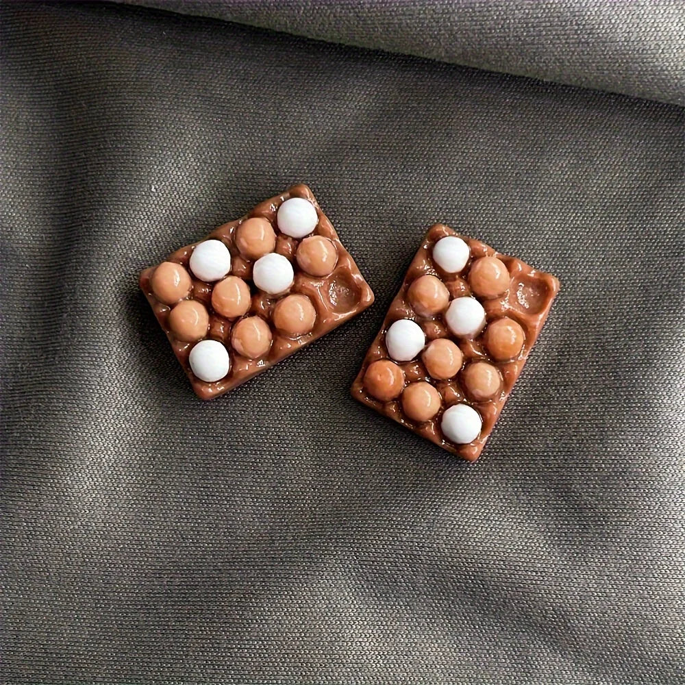 A set of brown chocolate-coated candies with white centers arranged in a diamond shape on a gray fabric background.