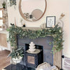 A decorative fireplace mantel decorated with a lush green eucalyptus wreath garland and potted plants.