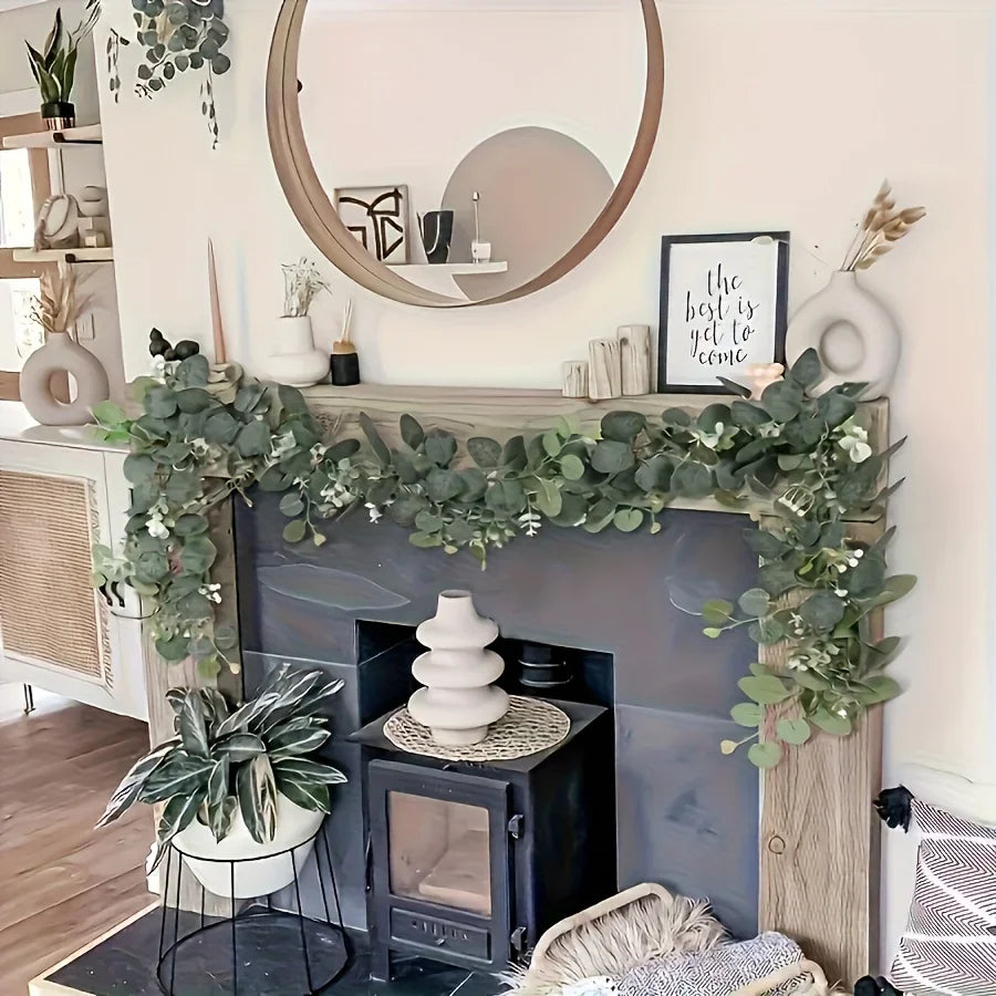 A decorative fireplace mantel decorated with a lush green eucalyptus wreath garland and potted plants.
