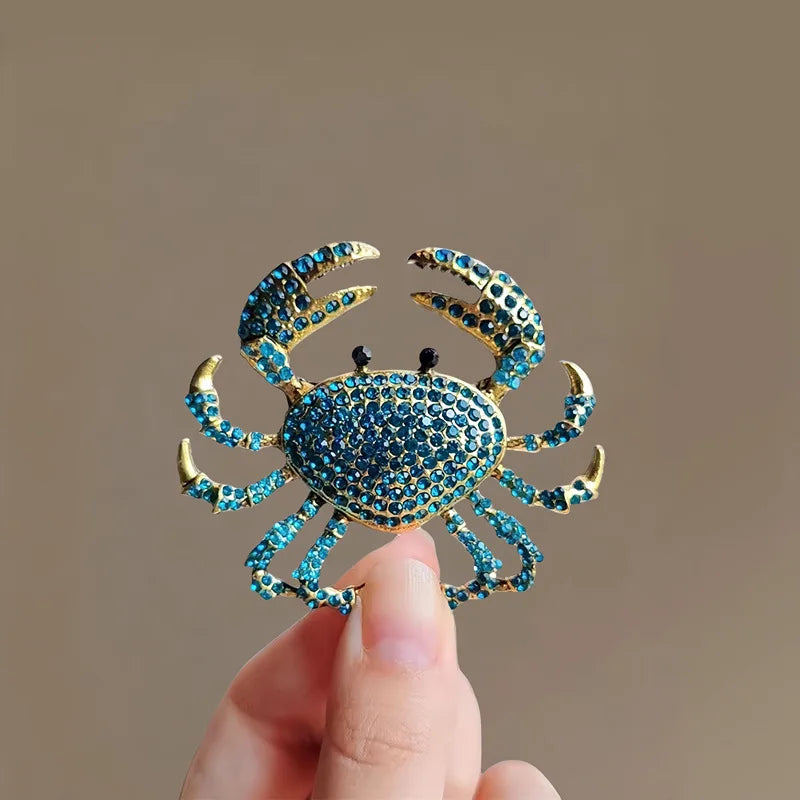 A hand holds a vintage marine life brooch pin set featuring a blue textured crab design.