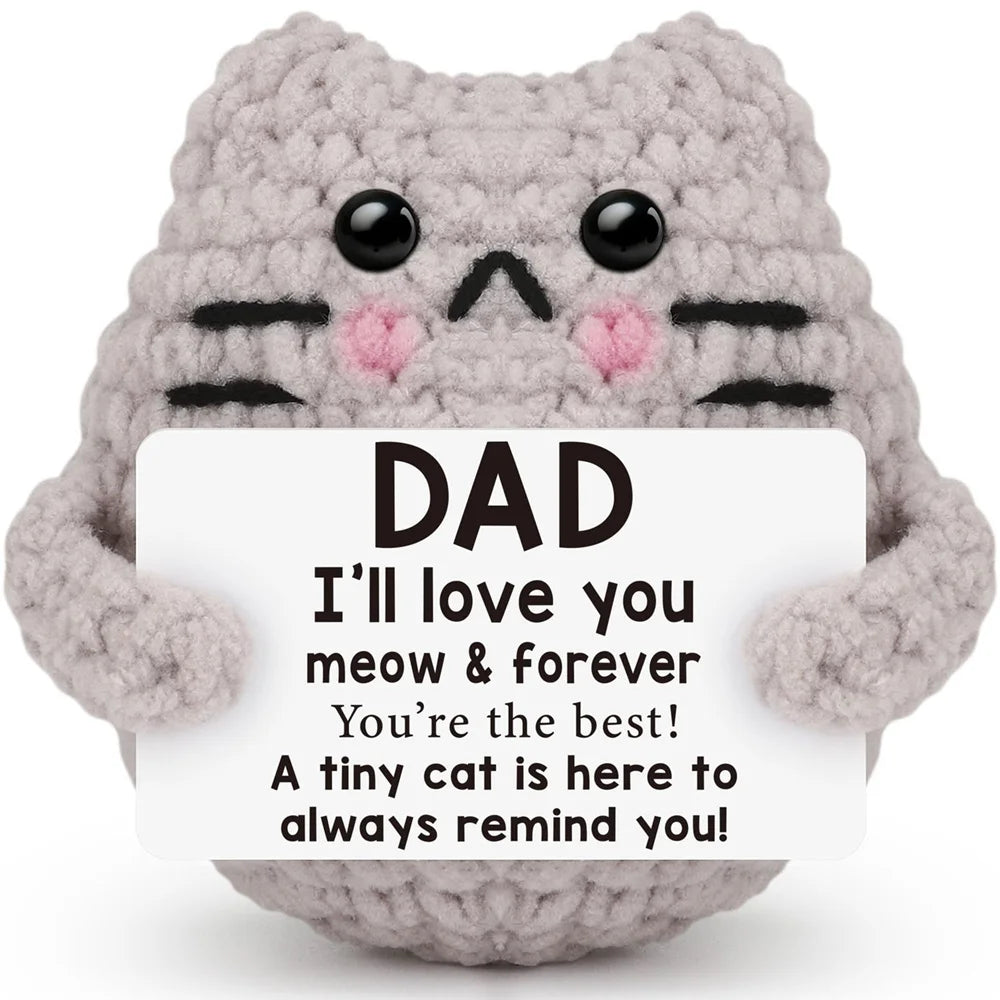 A handcrafted gray crochet cat doll with black stripes and pink accents, holding a card that says I'll love you dad.