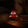 A red witch hat night light with a stained glass effect sits on a wooden surface next to a stack of books.