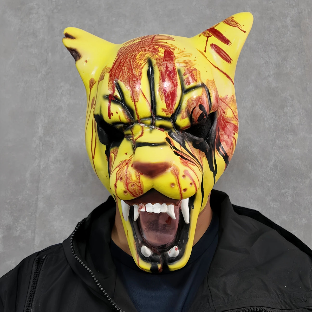 A yellow tiger horror latex mask with blood splatters and an open mouth, worn by a person.