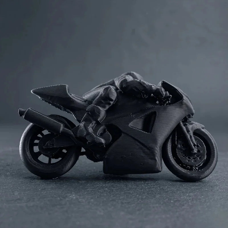 A black 3D printed racing motorcycle rider figurine displayed on a dark surface.