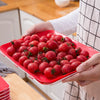 A hand holds a red tray filled with fresh cherry tomatoes on a wooden surface.