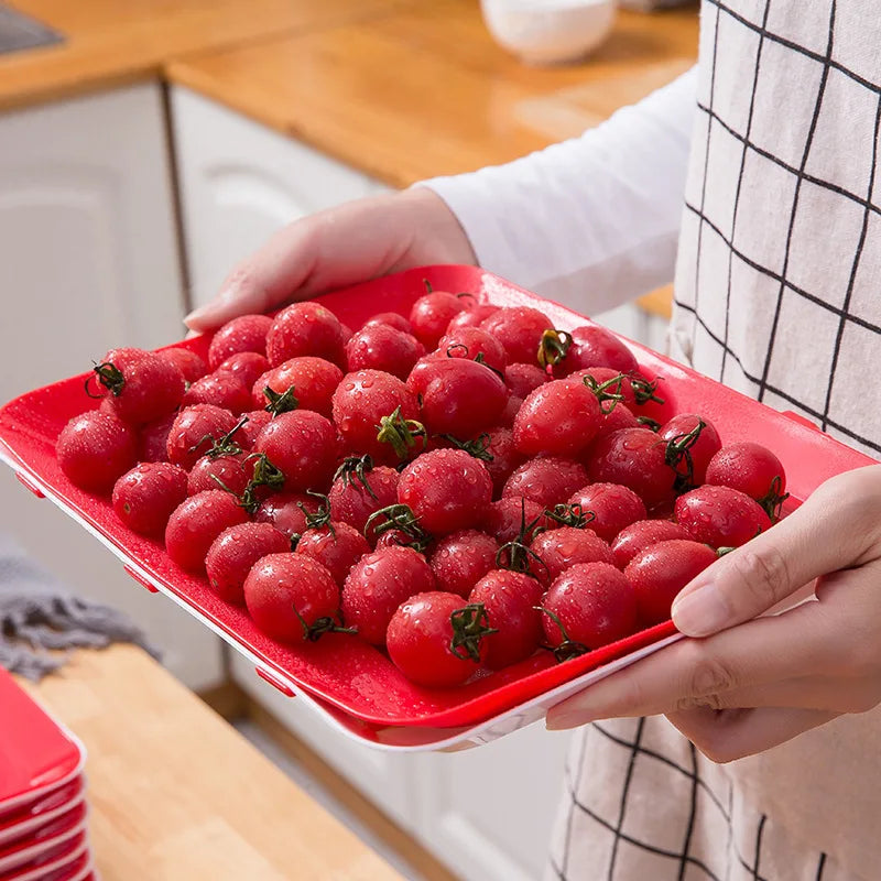 A hand holds a red tray filled with fresh cherry tomatoes on a wooden surface.