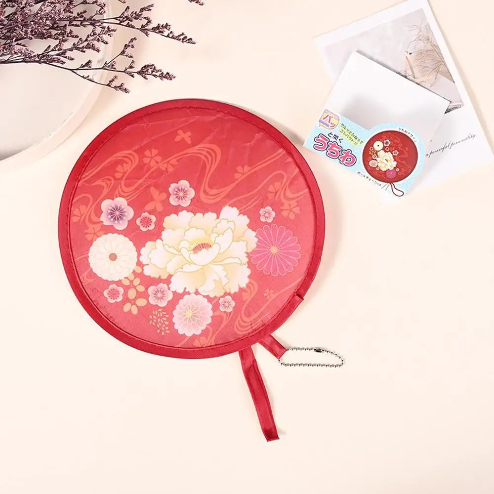 A red portable foldable cooling handheld fan with a decorative pattern is shown on a light background.