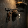 A set of two leather wall hooks with skull charms mounted on a dark gray textured wall.