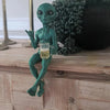 A resin statue of a green alien holding a glass of beer on a wooden surface.