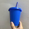 A hand holds a bright blue plastic cold cup with a lid and straw against a light gray wall.