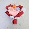 A handmade crochet sunflower mini bouquet featuring pink, yellow, and blue flowers wrapped in red paper.
