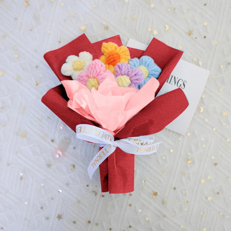 A handmade crochet sunflower mini bouquet featuring pink, yellow, and blue flowers wrapped in red paper.