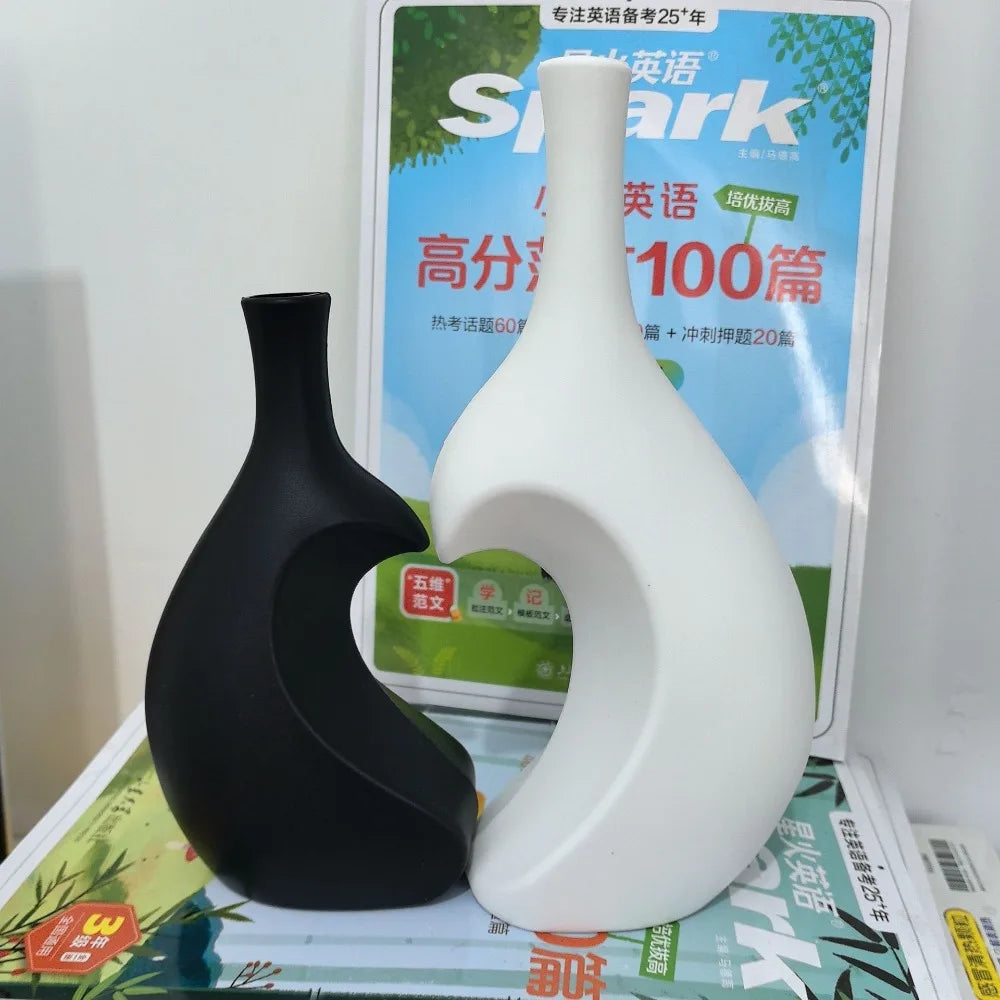 A black and white modern heart-shaped ceramic vase displayed in front of a product sign.