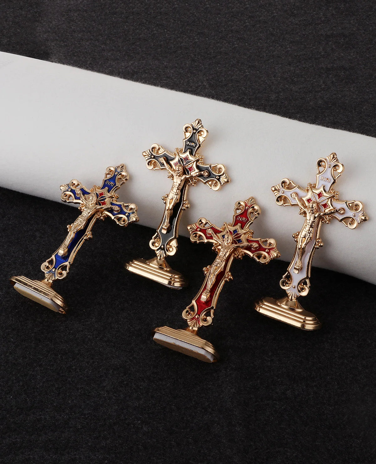 A set of four metal crucifix desk crosses with self-adhesive bases displayed on a dark surface.