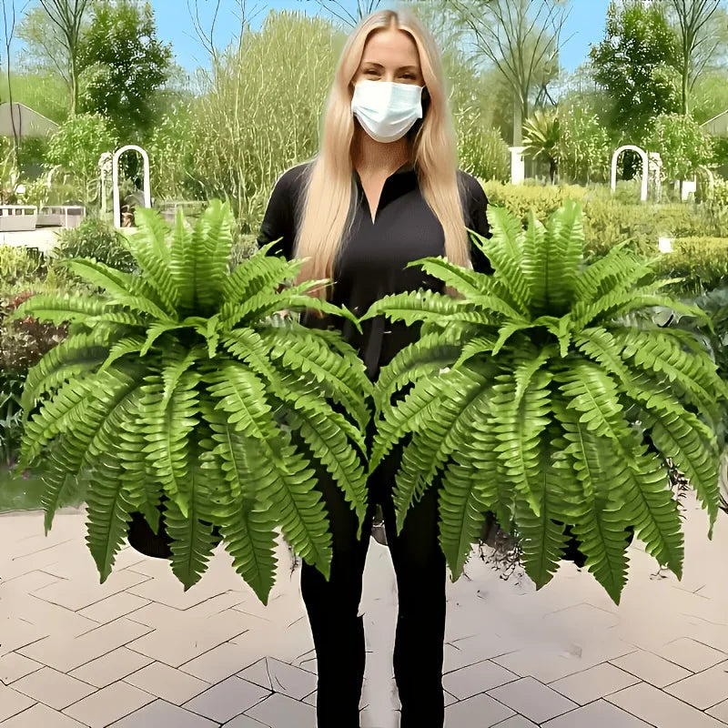 A woman stands in a garden holding two large artificial Boston ferns.