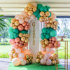 A floral arch made of metallic latex balloons in shades of pink, peach, and teal for a party decoration.