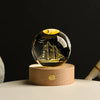 A spherical crystal ball night light with a golden ship design rests on a natural wooden base.