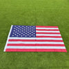 A double-sided American flag with red, white, and blue stripes and stars laid flat on green grass.