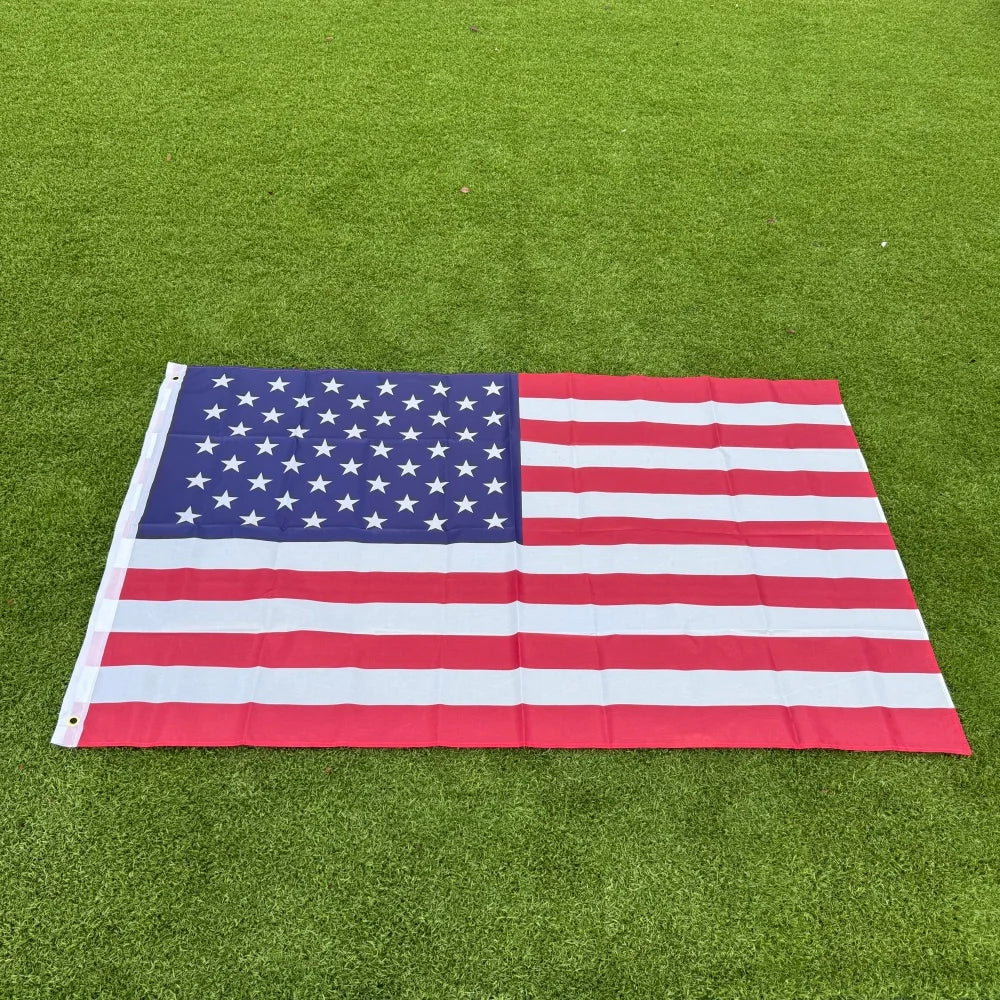 A double-sided American flag with red, white, and blue stripes and stars laid flat on green grass.