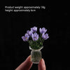 A hand holds a small glass vase filled with purple lilac flowers for home decor.