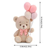 A cute teddy bear figurine with pink ball decorations on its ears and a pink bow.