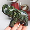 A hand holds a natural jade elephant carving statue with green and black mottled color.