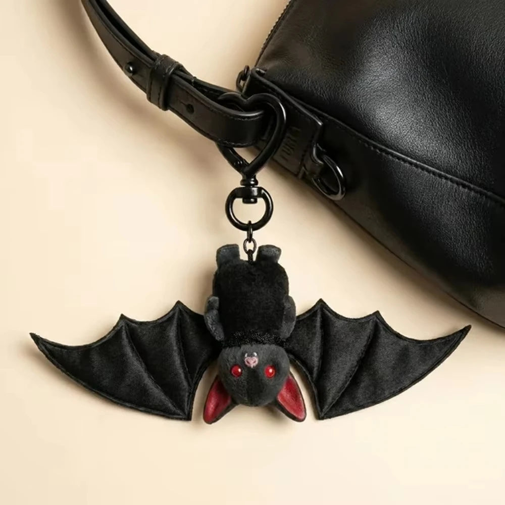 A black plush bat keychain with translucent wings attached to a leather strap and ring.