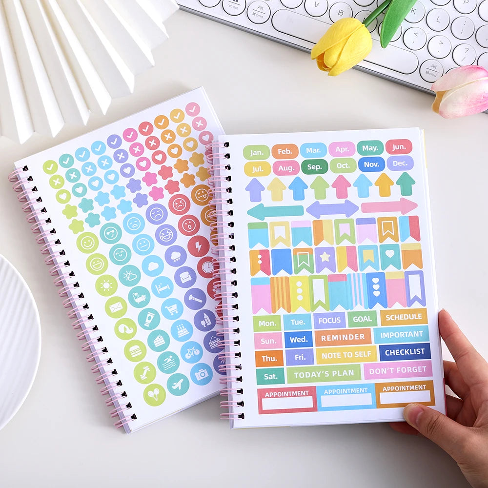 A spiral-bound self-care journal with colorful monthly planner pages and stickers is shown on a white surface.
