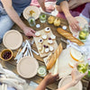 Hands are serving food from disposable paper plates on a wooden table.