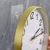 A round gold-rimmed clock with a white face and black numbers is mounted on a gray marble wall.