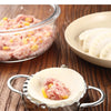 A close-up of a stainless steel dumpling maker with a crimped edge, holding pink meat filling.
