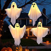 Three glowing white ghost decorations hanging from a tree in a suburban yard during Halloween night