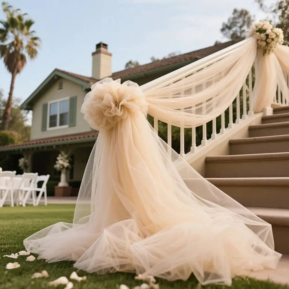 A sheer beige tulle fabric with a ruffled neckline and long drape is displayed on a grassy lawn next to stone stairs.